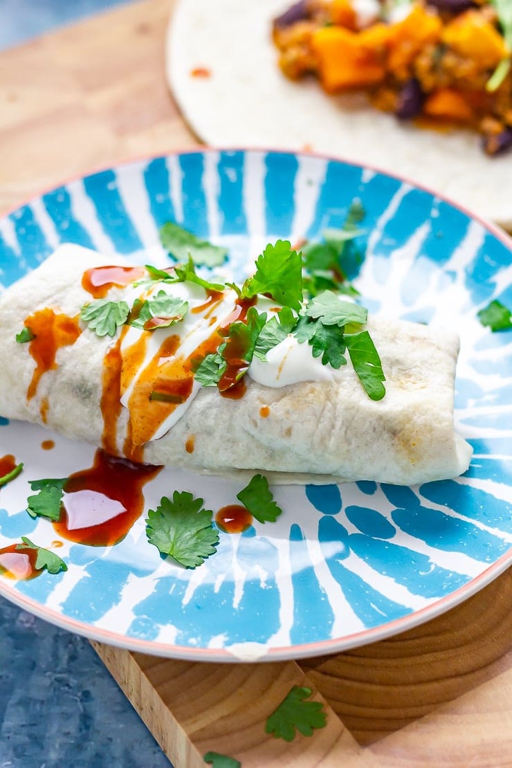 Turkey burrito on a plate with hot sauce on a wooden board