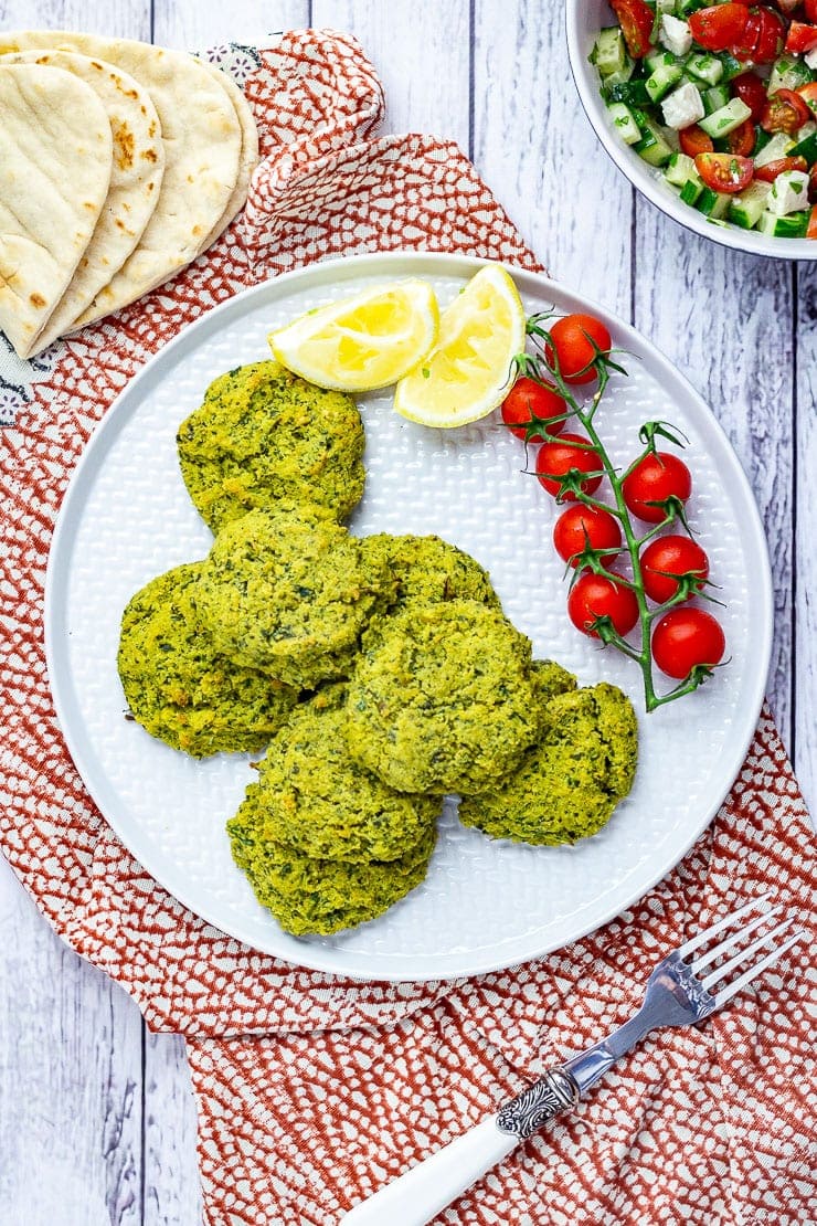 Overhead shot of baked falafel with cherry tomatoes and lemon slices on a patterned cloth