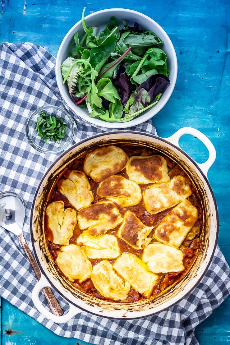 Overhead shot of tomato and halloumi bake on a check background with salad