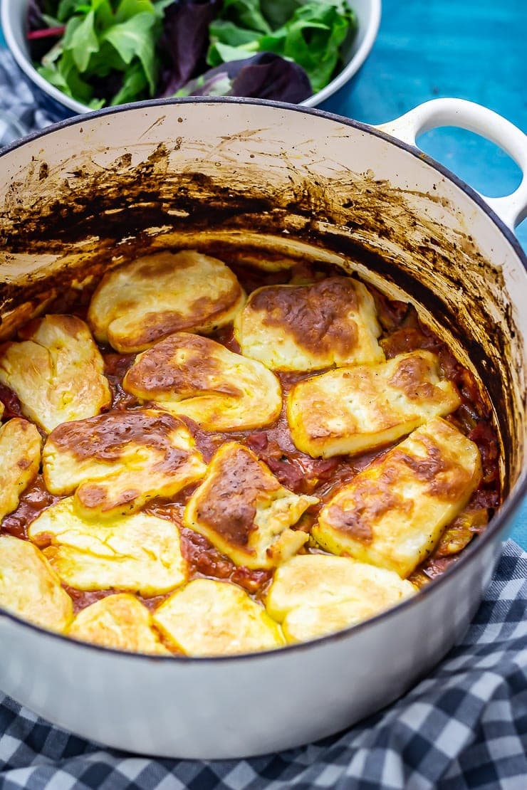 Tomato and halloumi bake on a checked background with salad in the background