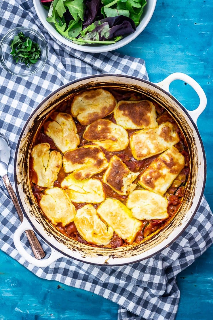 Overhead shot of tomato and halloumi bake on a checked cloth over a blue background