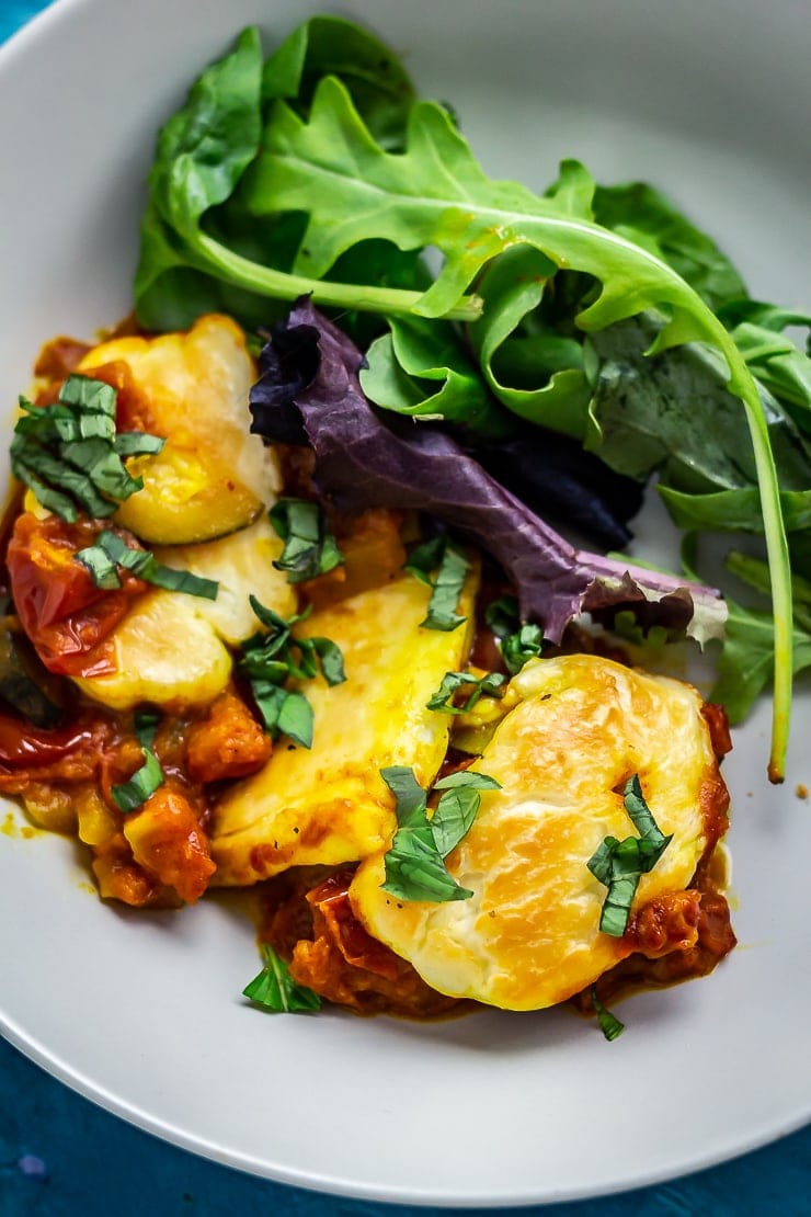 Close up of tomato and halloumi bake in a bowl with salad