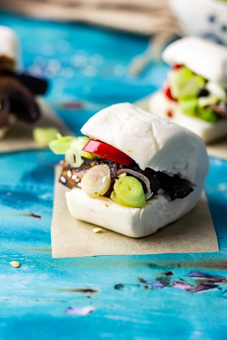 Close up of mushroom bao on a blue background with chilli and spring onion