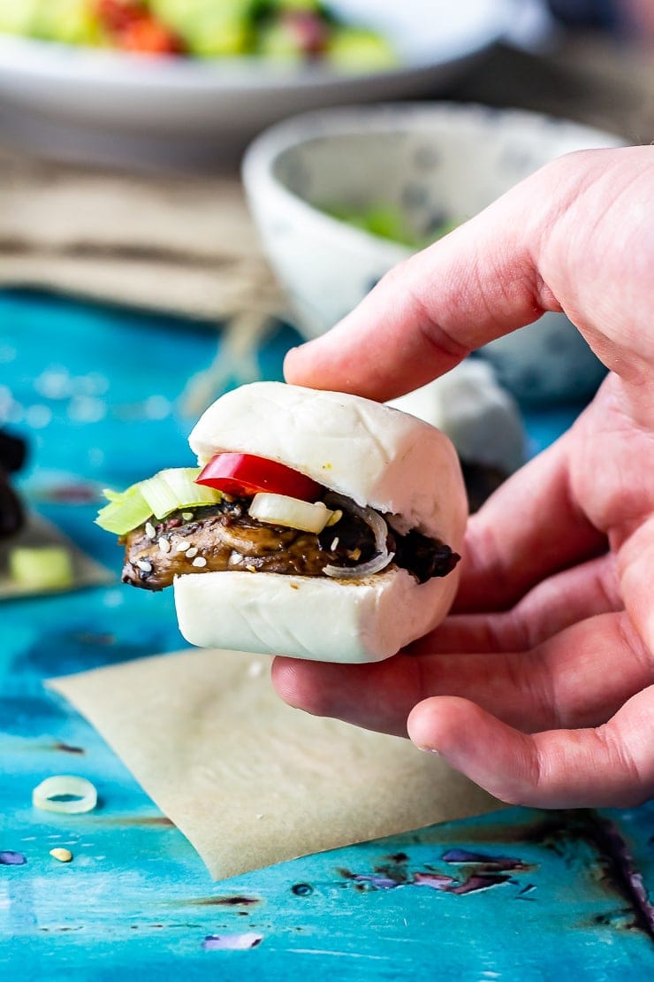 Hand holding a mushroom bao with a blue background