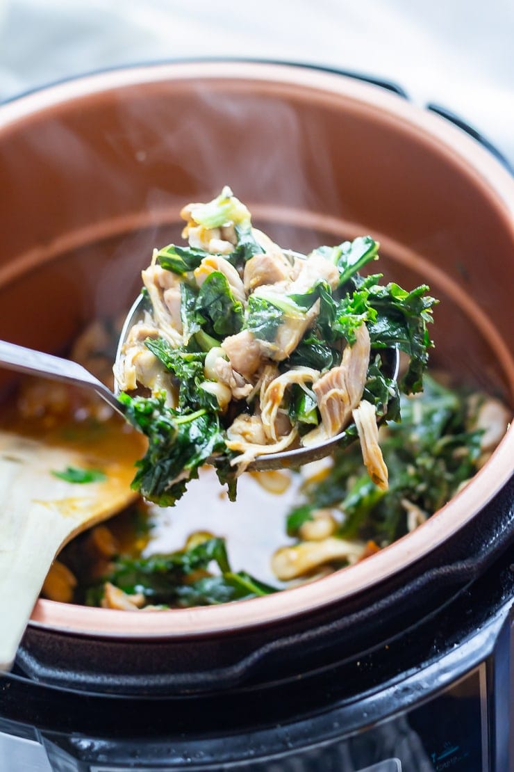 Ladleful of chicken casserole with kale and white beans over a pressure cooker