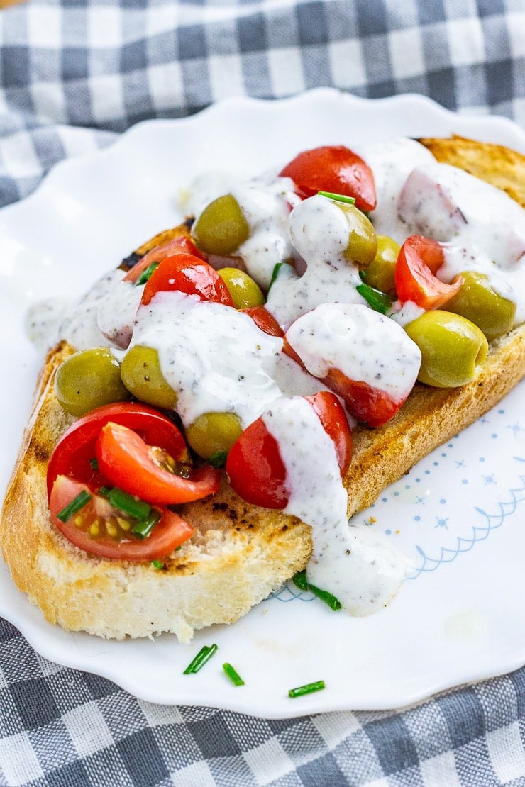 Olive and tomatoes on toast on a white plate on a checked cloth