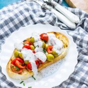 Olive and tomatoes on toast on a white plate on a checked cloth