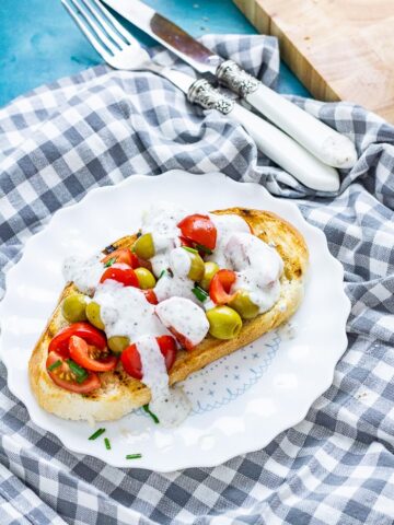 Olive and tomatoes on toast on a white plate on a checked cloth