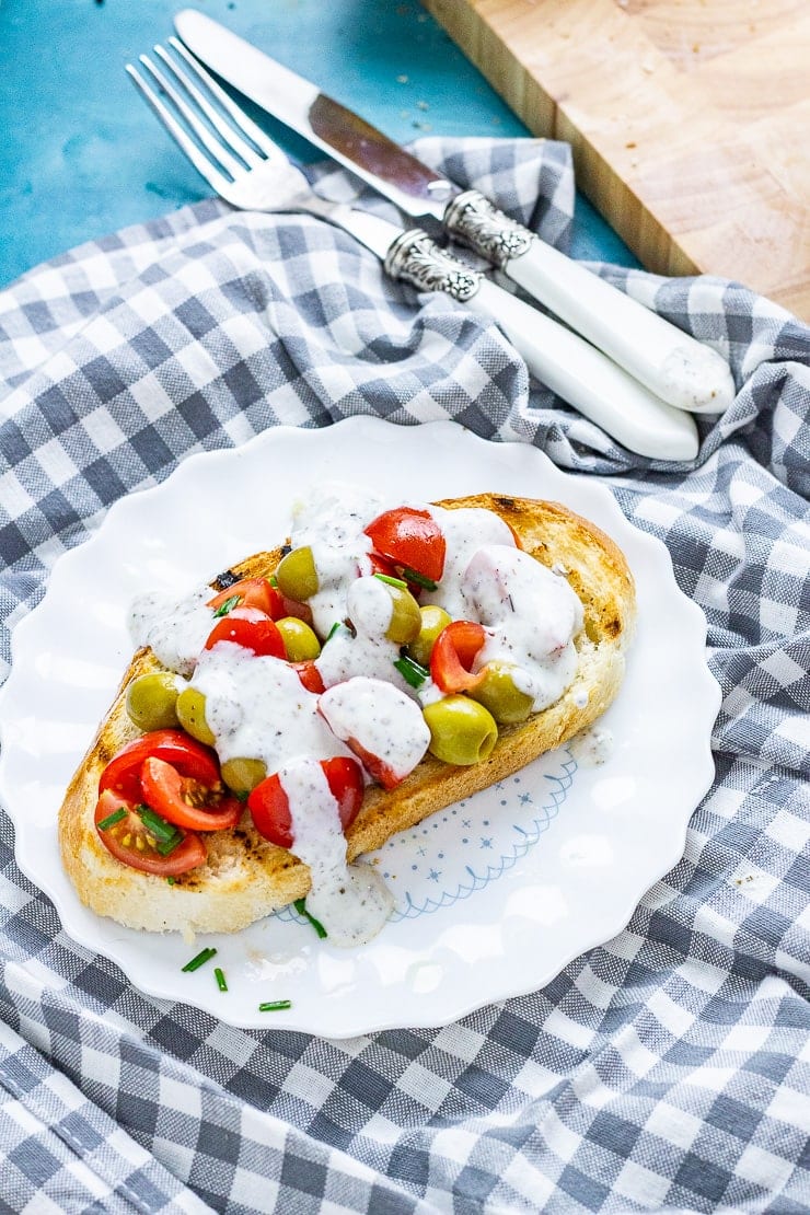 Olive and tomatoes on toast on a white plate on a checked cloth