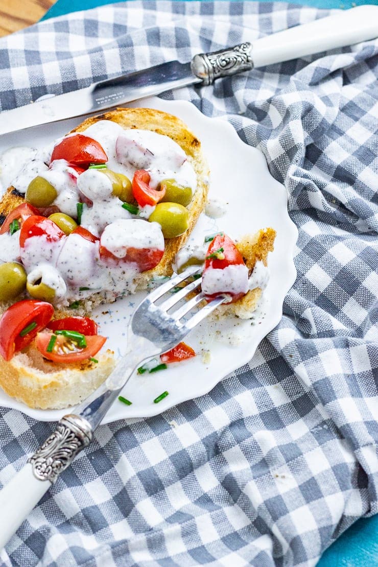 Olives and tomatoes on toast with dressing on a plate with a fork on a checked cloth