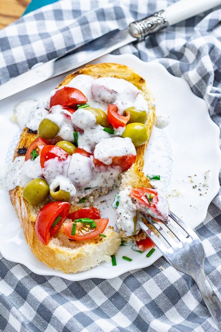 Olives and tomatoes on toast with dressing on a plate with a fork on a checked cloth