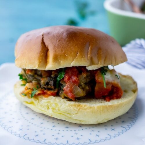 Side on shot of vegetarian meatball sandwich on a white plate over a blue background