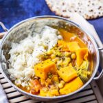 Bowl of pressure cooker coconut curry on a wooden tray with bread in the background