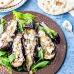 Aubergine Recipes | Overhead shot of baked aubergine with tahini on a platter with flatbread on a blue background