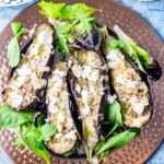 Overhead shot of baked aubergine with tahini and goat's cheese with lettuce leaves on a blue background