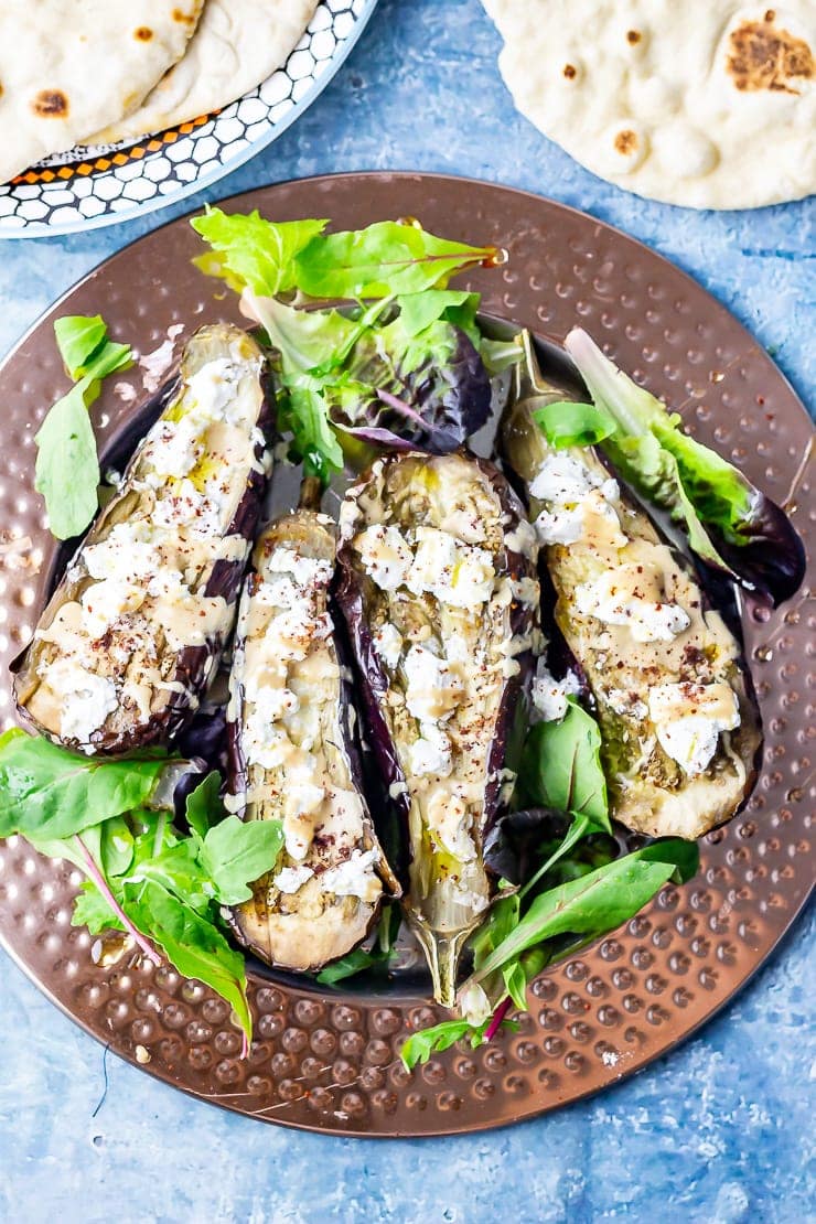 Overhead shot of baked aubergine with tahini and goat's cheese with lettuce leaves on a blue background