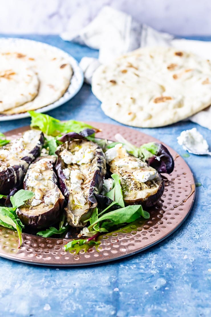 Side on shot of baked aubergine with tahini and goat's cheese on a blue background