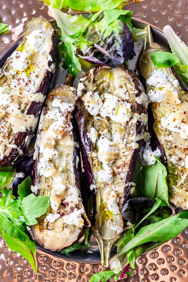 Close up shot of baked aubergine with tahini and goat's cheese with salad leaves on a platter