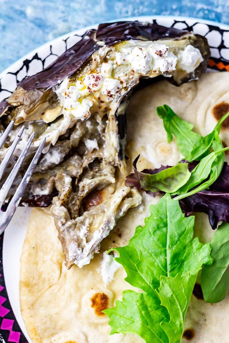 Baked aubergine with a fork on a plate with flatbread