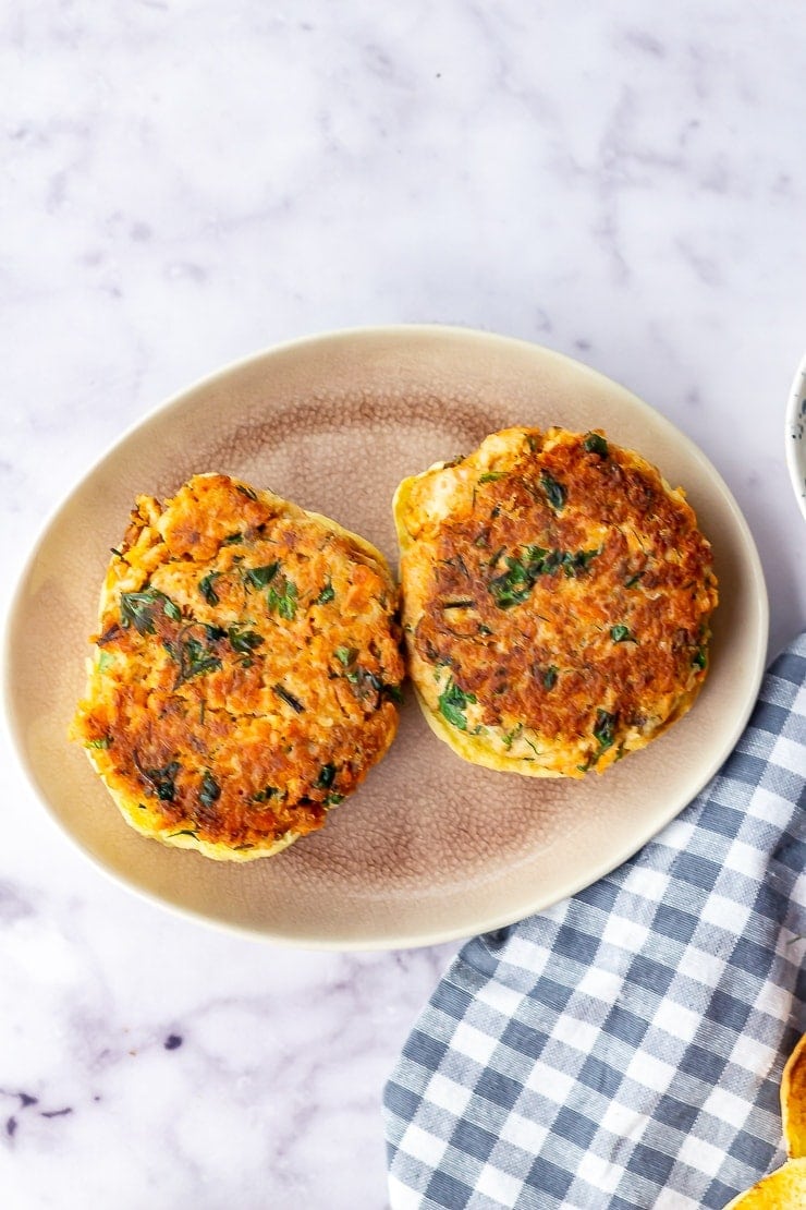 Overhead shot of two salmon burgers on a pink plate with a checked cloth over a marble background