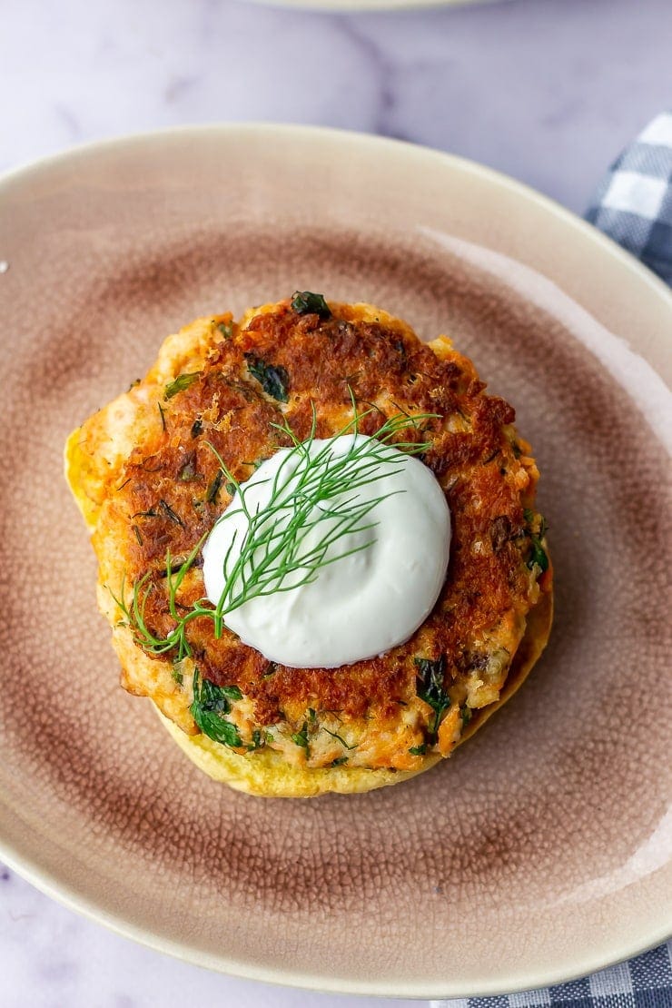 Overhead shot of a salmon burger with garlic yoghurt on a pink plate over a marble background