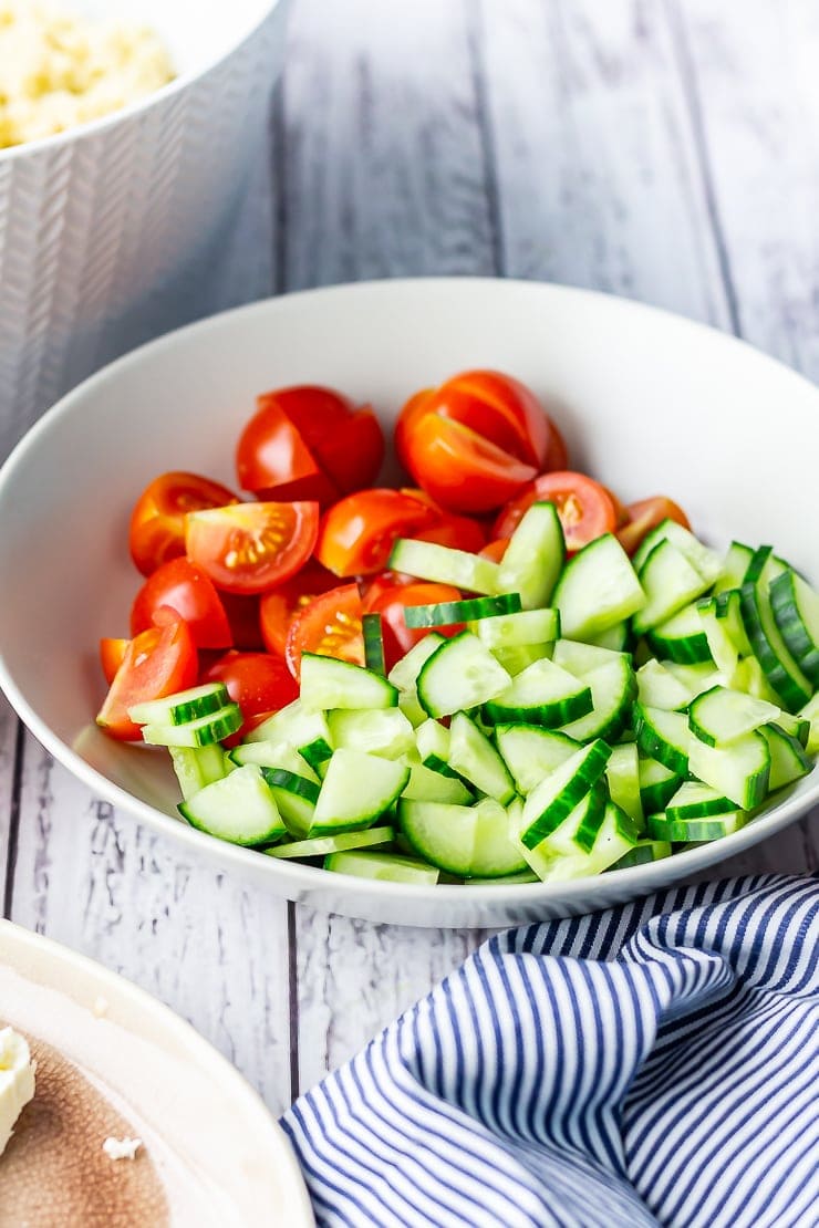 Bowl of sliced cucumber and tomato for summer salad on a white wooden background