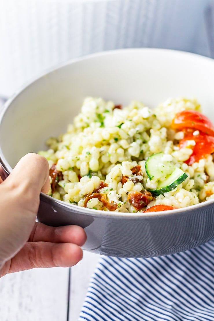 Hand holding a bowl of summer salad with pearl barley 