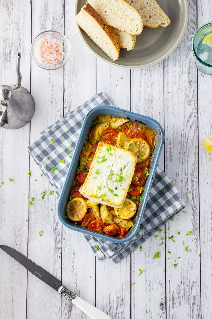 Overhead shot of baked feta on a checked cloth over a white wooden background