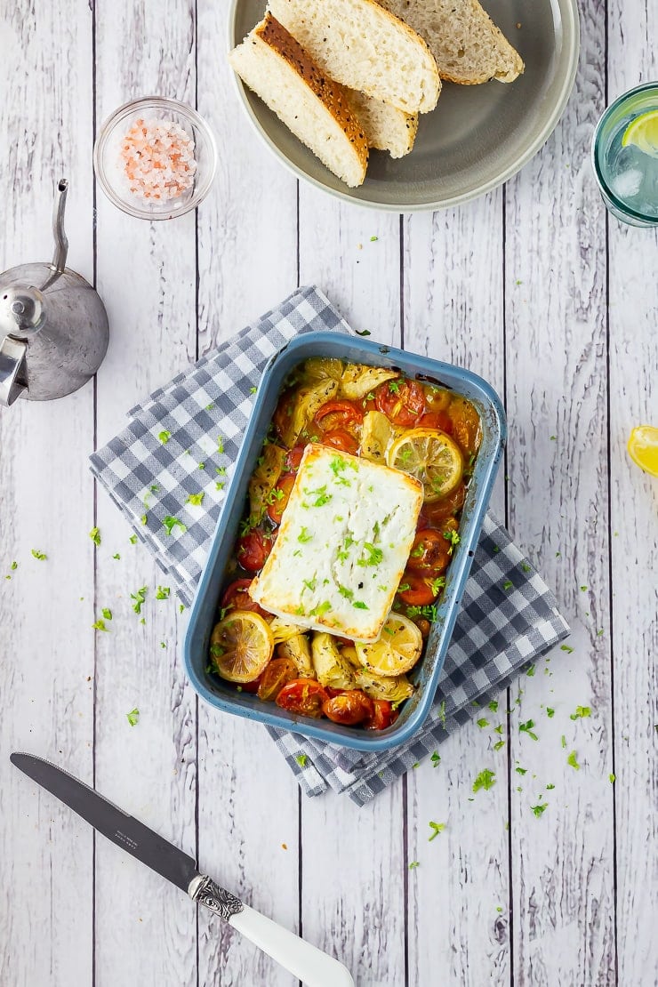 Overhead shot of baked feta on a checked cloth over a white wooden background