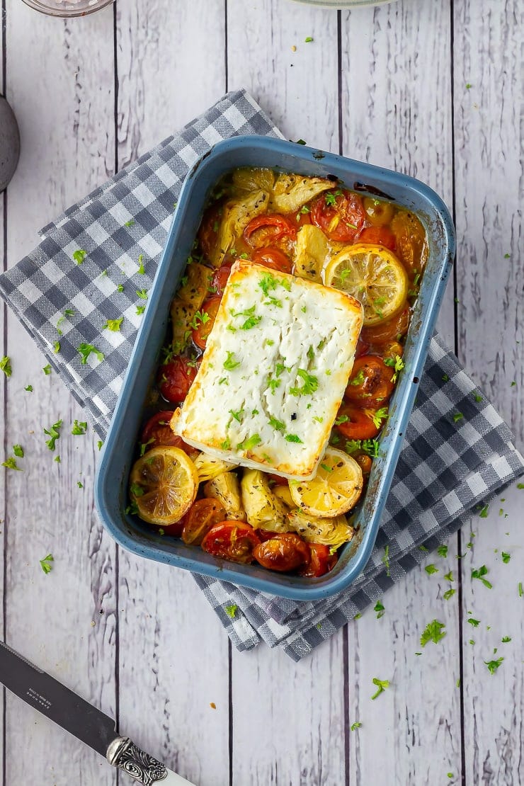 Overhead shot of baked feta with vegetables in a blue baking dish on checked cloth