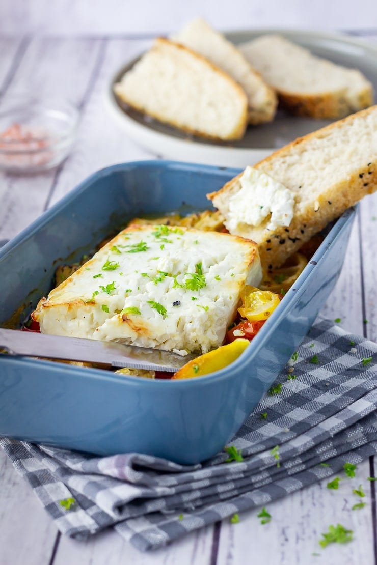 Baked feta in a blue baking dish on a checked cloth