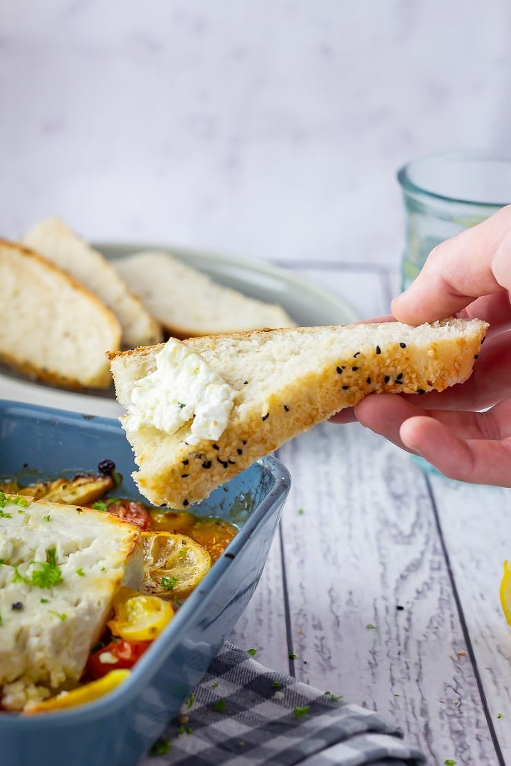 Hand holding a slice of bread with baked feta spread on it