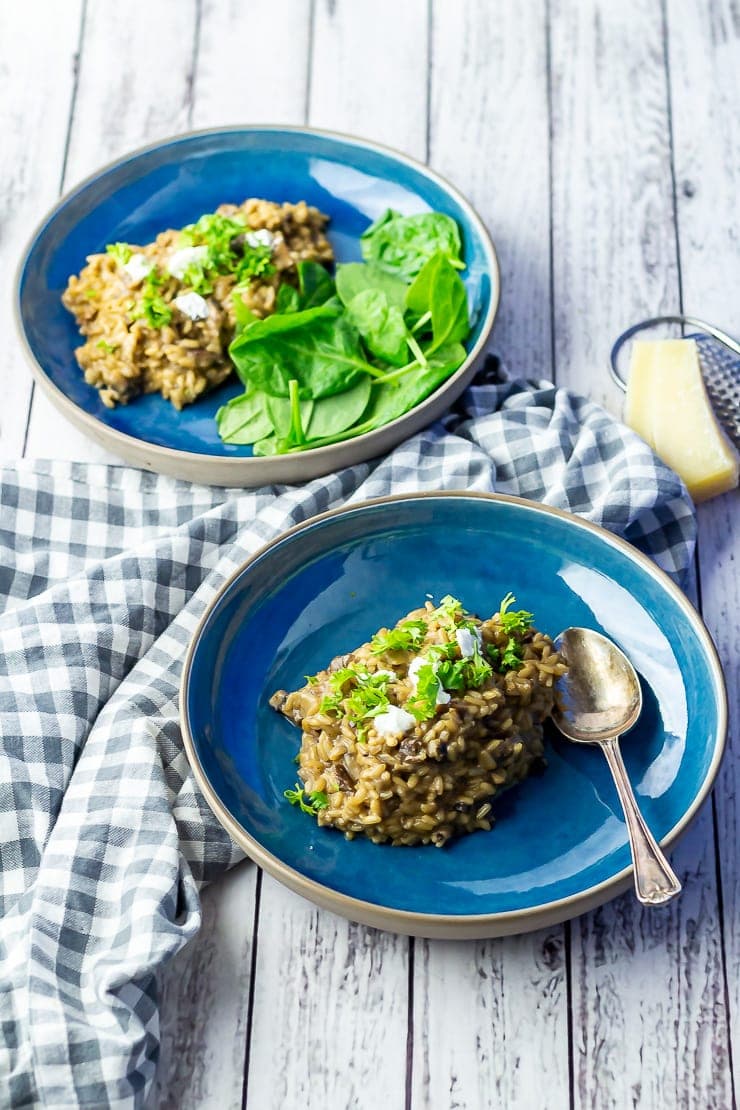 Two bowls of black garlic risotto on a white wooden background with a checked cloth