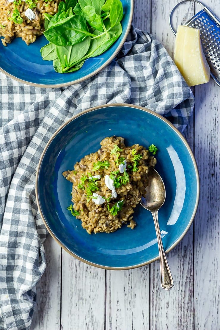 Overhead shot of black garlic risotto in a blue bowl on a white wooden background