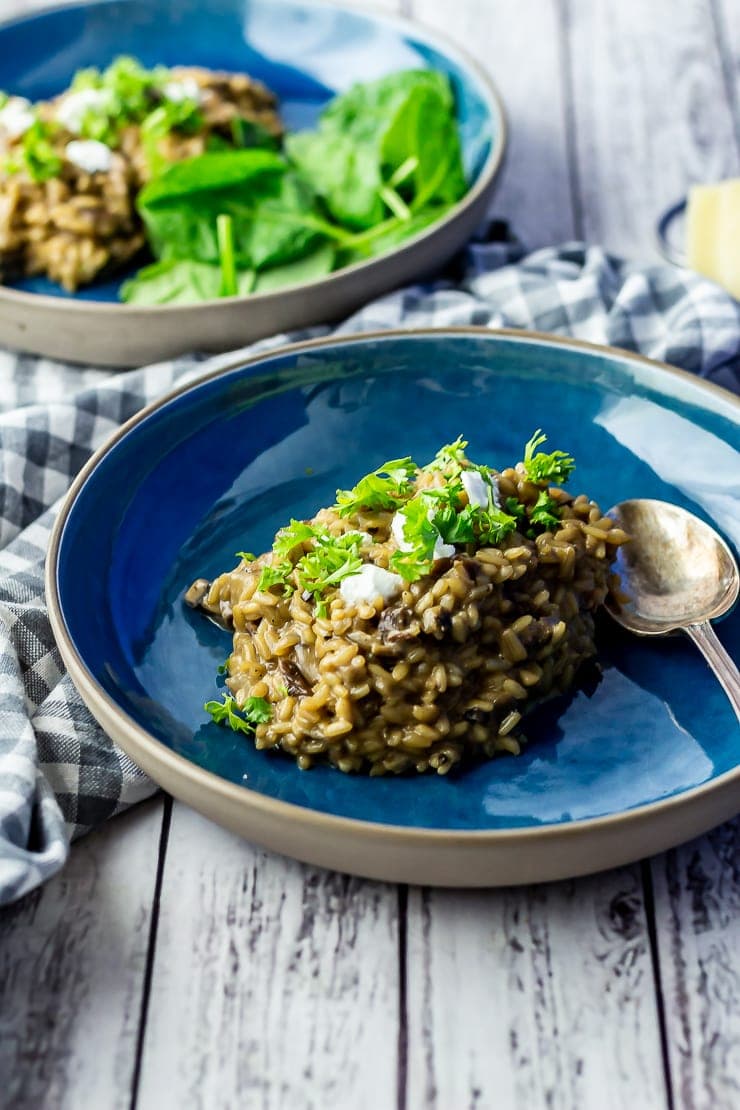 Black garlic risotto in a blue bowl on a white wooden background