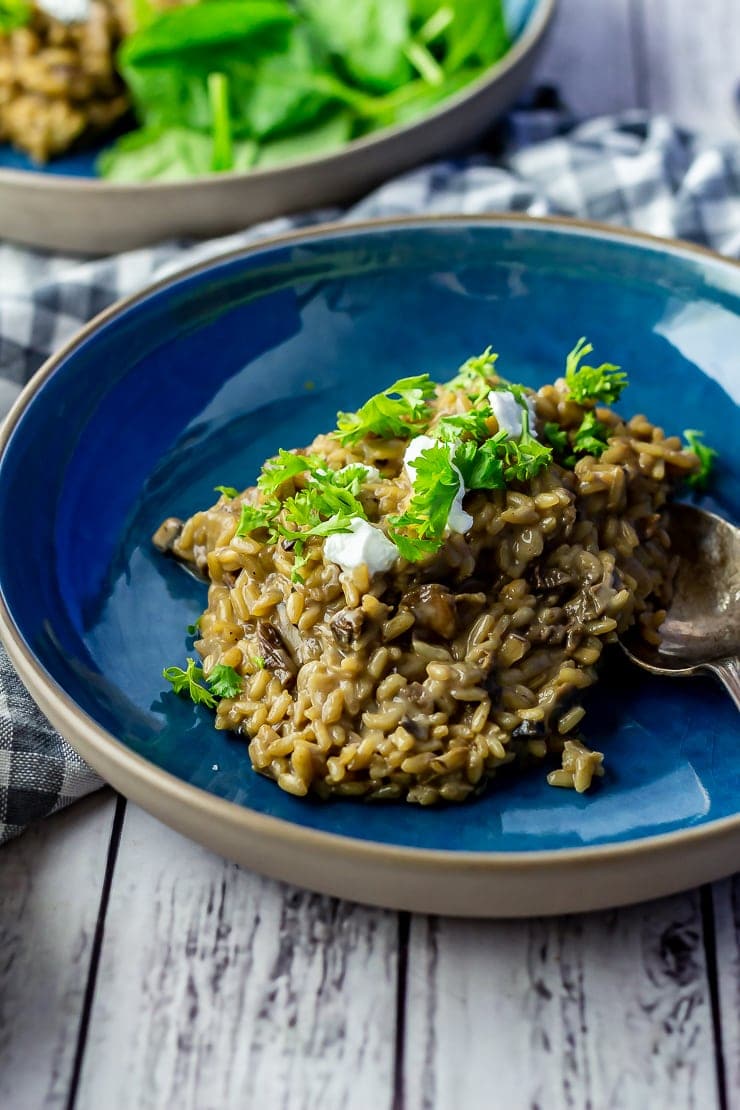 Bowl of black garlic risotto in a blue bowl topped with goat's cheese and parsley