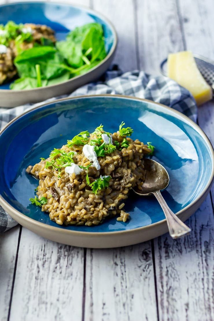 Side on shot of black garlic risotto in a blue bowl on a white wooden background