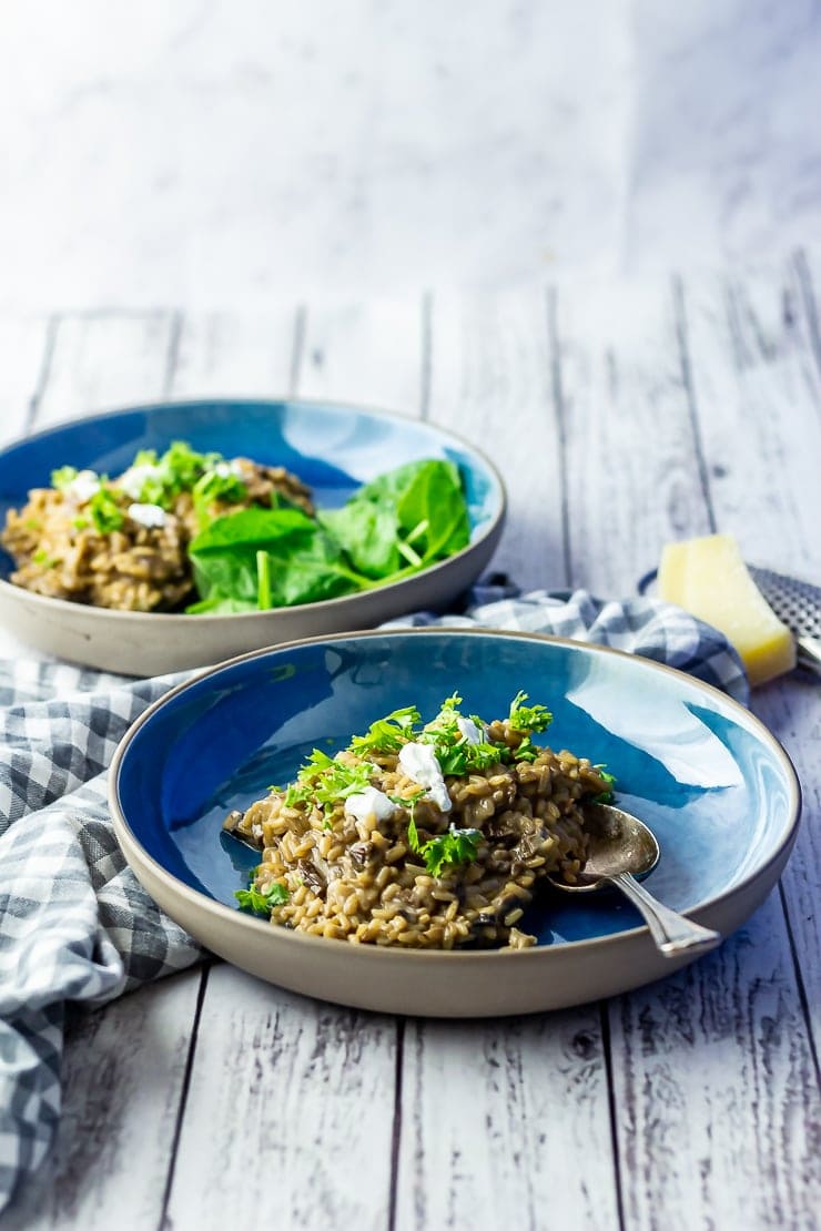 Two bowls of black garlic risotto on a white wooden background 