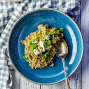 Overhead shot of black garlic risotto in a blue bowl on a white wooden background