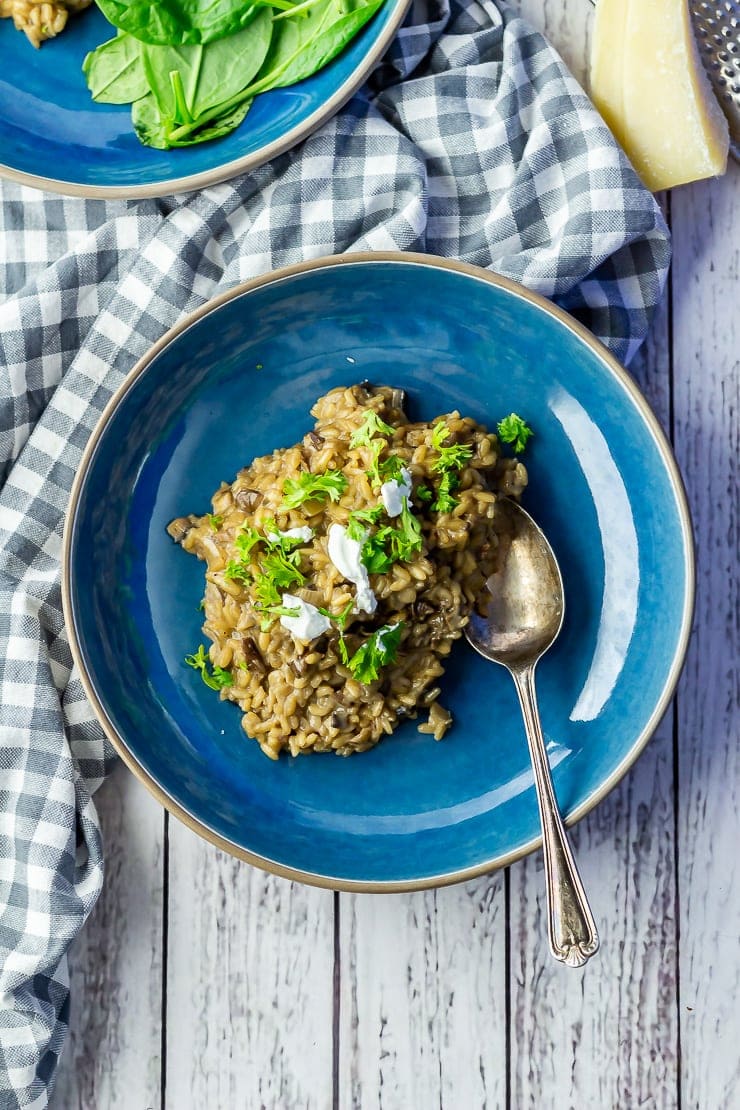 Overhead shot of black garlic risotto in a blue bowl on a white wooden background