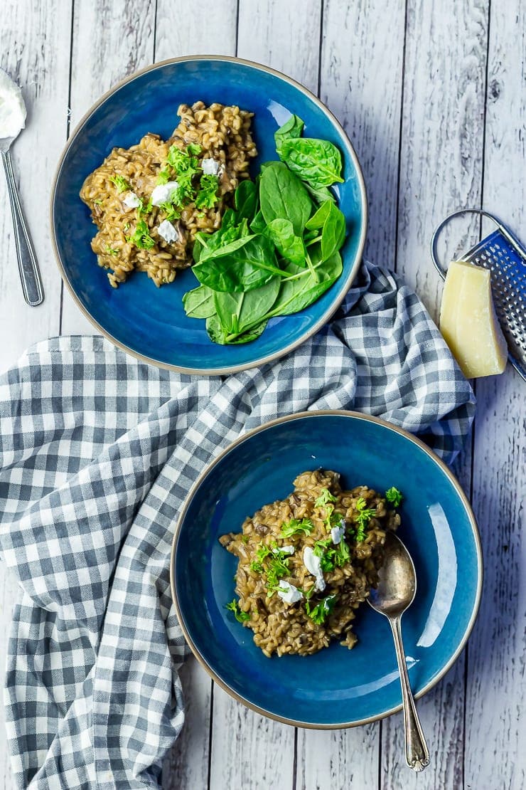 Overhead shot of two blue bowls of black garlic risotto on a white wooden background with a checked cloth