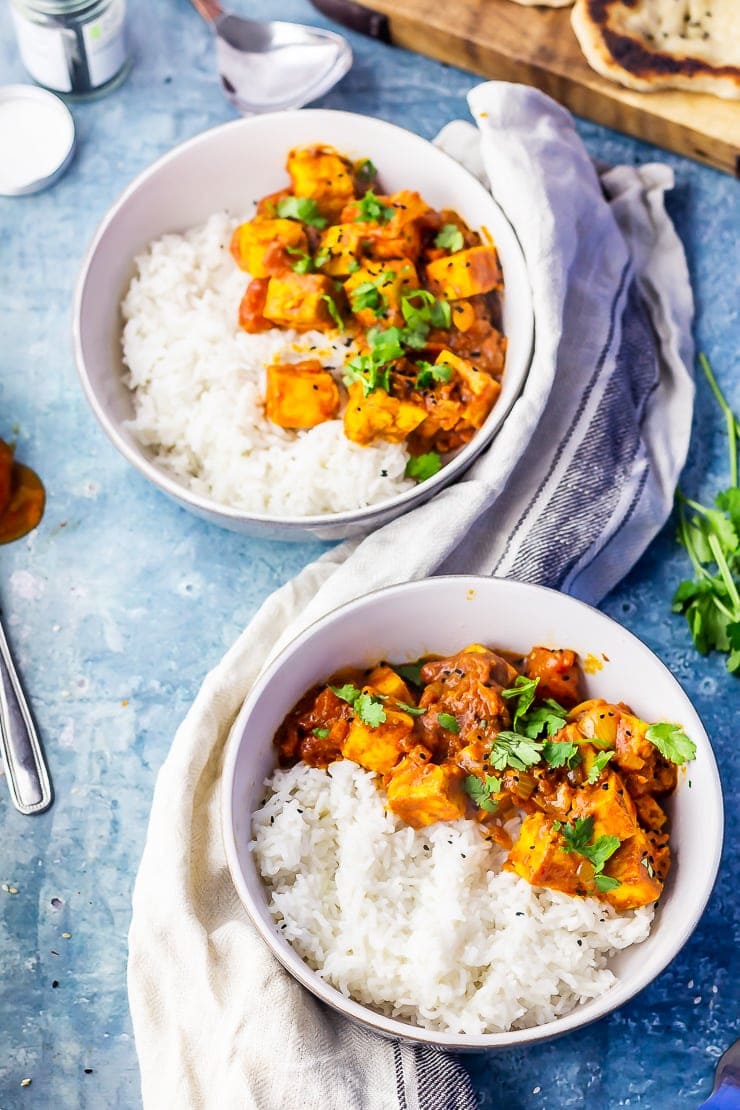 Overhead shot of two bowls of paneer tikka masala on a blue background with a cloth