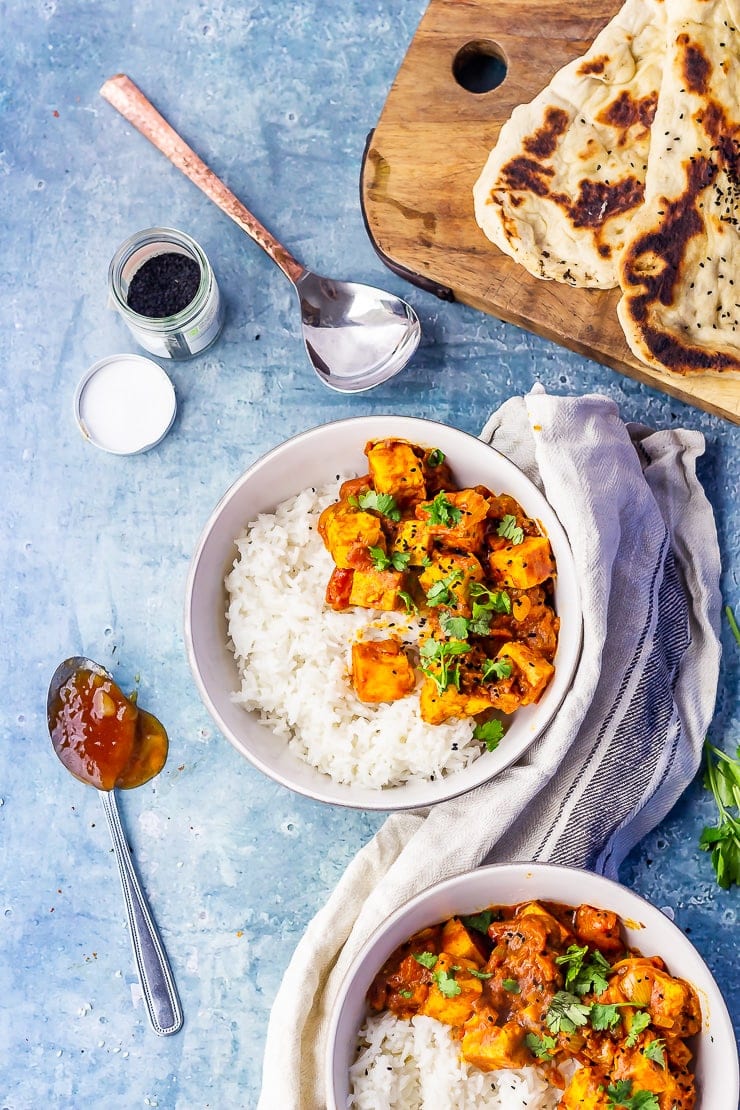 Overhead shot of paneer tikka masala on a blue background with naan bread 