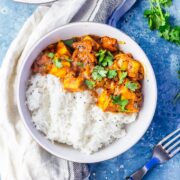 Overhead shot of paneer tikka masala on a blue background with a cloth and fork