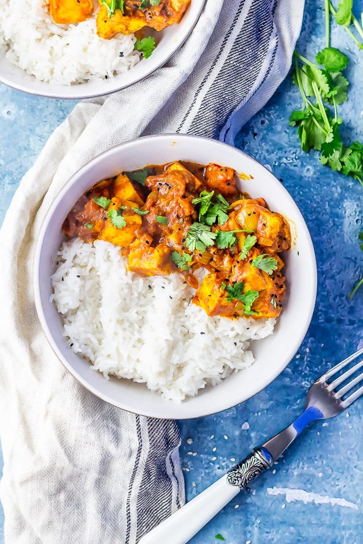 Overhead shot of paneer tikka masala on a blue background with a cloth and fork