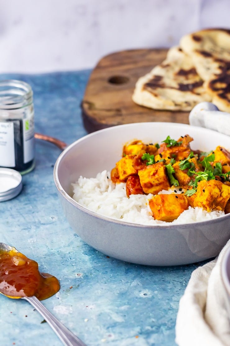 Side on shot of paneer tikka masala on a blue background with a spoonful of mango chutney