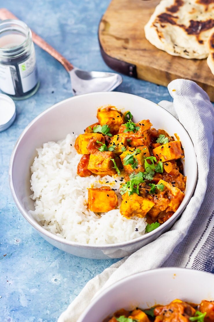 Side on shot of paneer tikka masala on a blue background with a cloth