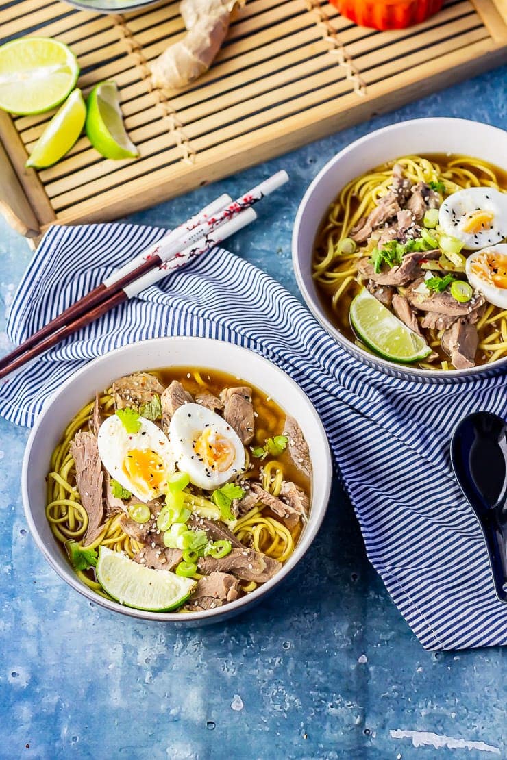 Two bowls of leftover turkey soup with noodles on a blue background with a striped cloth