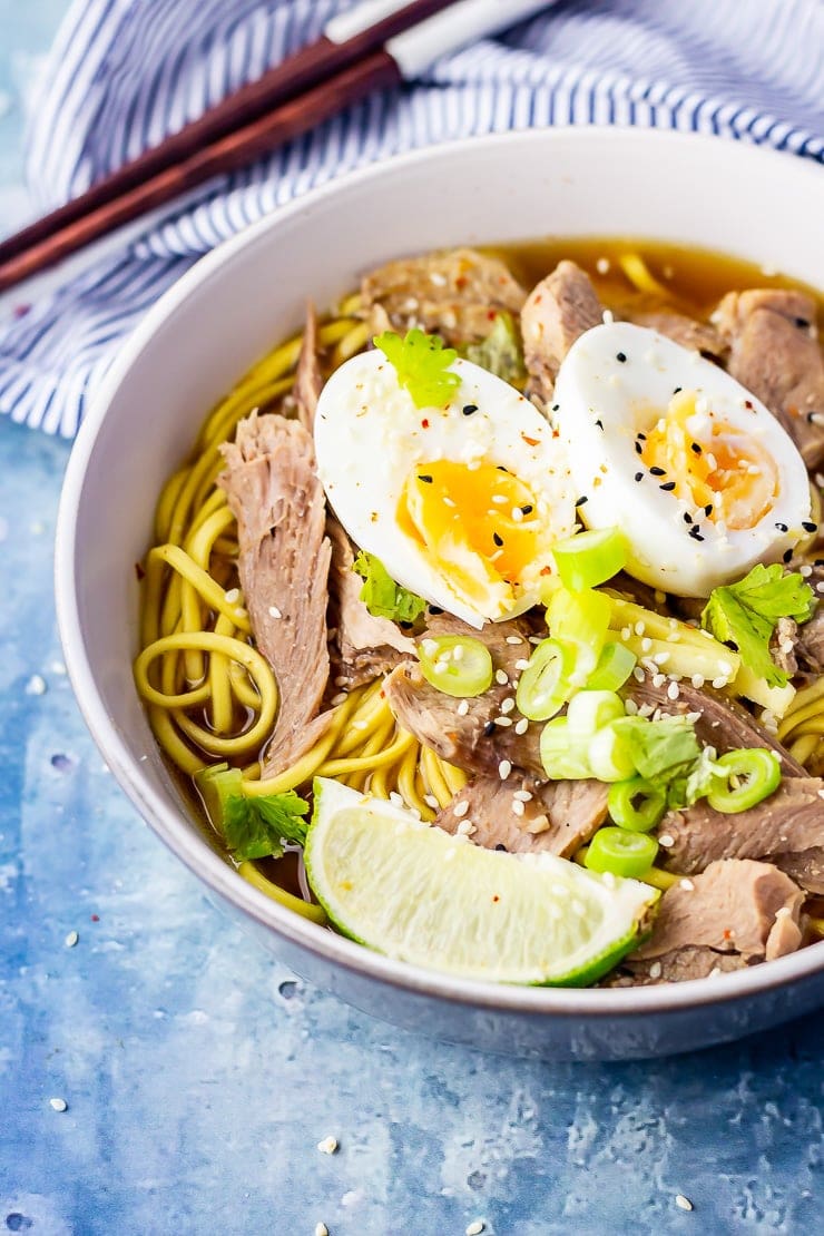 Bowl of leftover turkey soup with noodles on a blue background with a striped cloth