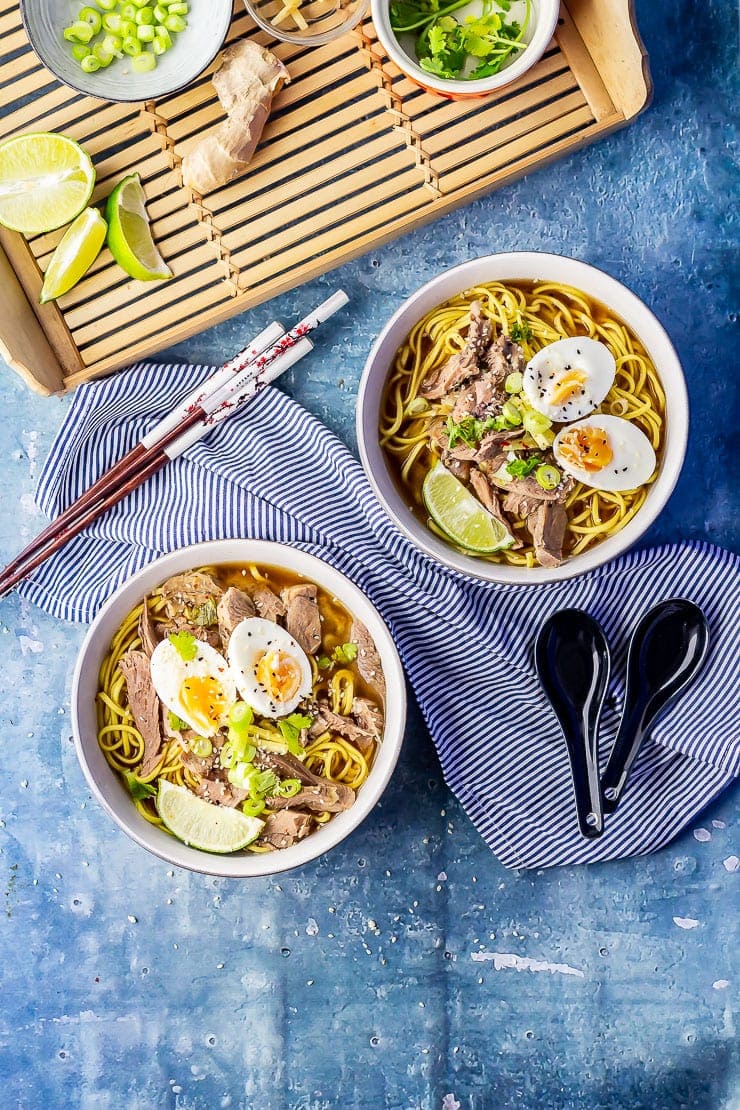 Overhead shot of two bowls of leftover turkey soup with noodles on a blue background with a striped cloth